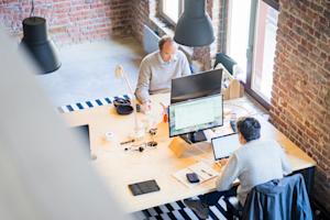 Two workers on their computers at their desks in an office.