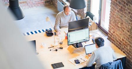 Two workers on their computers at their desks in an office.