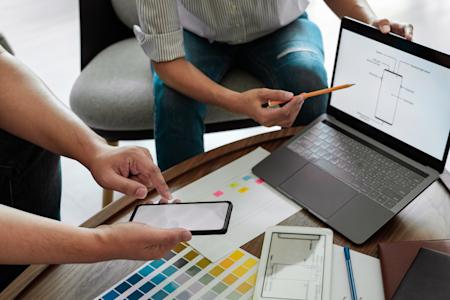 Two professionals collaborating on device management strategies with a laptop and smartphone, representing the efficiency of Autonomous Endpoint Management (AEM).