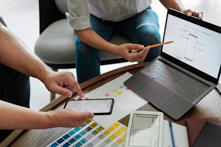 Two professionals collaborating on device management strategies with a laptop and smartphone, representing the efficiency of Autonomous Endpoint Management (AEM).