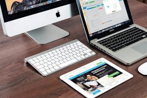 A computer, tablet, and laptop on a desk with multiple apps open.