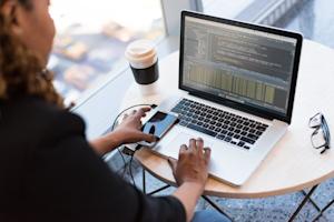 Woman coding on a laptop sitting at a coffee table.