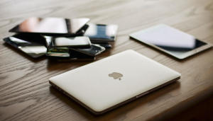 A pile of laptops, tablets, and mobile devices on a desk.