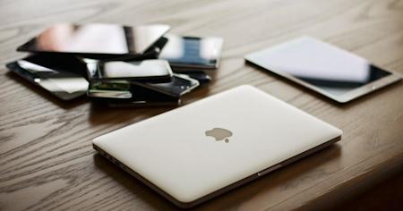 A pile of laptops, tablets, and mobile devices on a desk.
