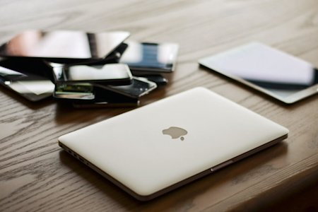 A pile of laptops, tablets, and mobile devices on a desk.