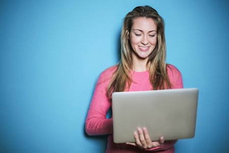 A woman smiling with her laptop in front of a blue background