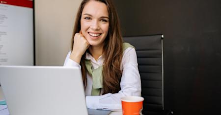 A woman smiling while working on a laptop.
