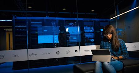 A woman working on her laptop next to a server room.