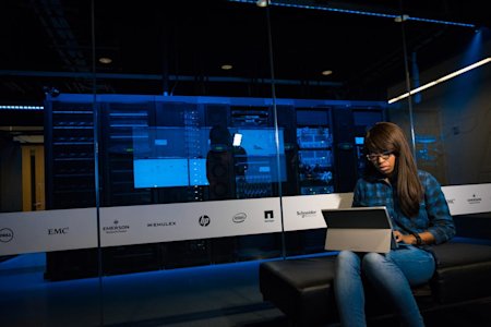 A woman working on her laptop next to a server room.