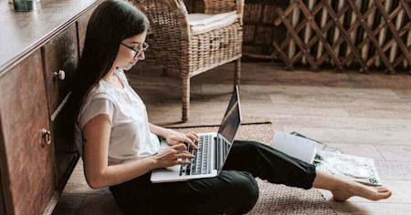 A woman sitting on the floor using her laptop with Splashtop remote access software to work remotely.