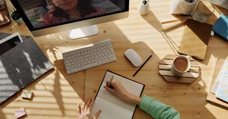 Writing in a notebook at a desk while looking at a computer