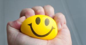 Stressed individual squeezing a stress ball with a happy face