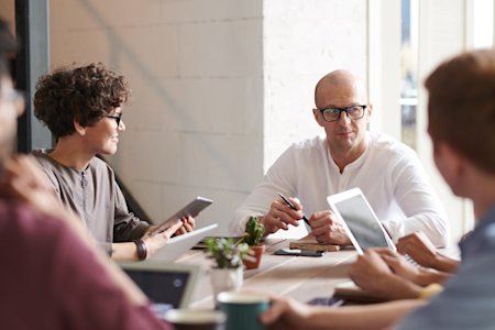 A group of coworkers talking at a conference table while working on their devices.