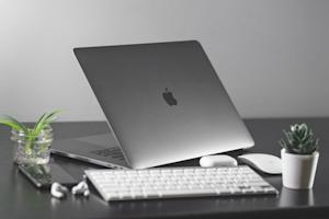 A Mac laptop, keyboard, mouse, and other items sitting on an office desk.