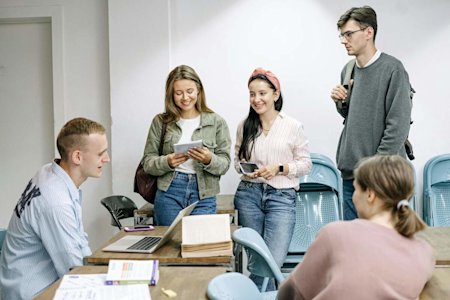 A group of students sitting in a classroom with various digital devices.
