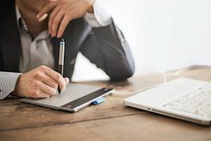 A graphic designer sitting at a tablet connected to a laptop while working remotely