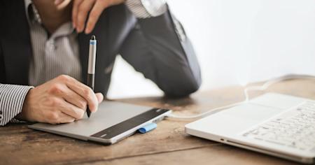 A graphic designer sitting at a tablet connected to a laptop while working remotely