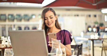 A happy woman working remotely at an outdoor restaurant by using Splashtop remote desktop software on her laptop.