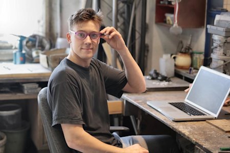 An IT help desk technician smiling in front of his computer at his desk.