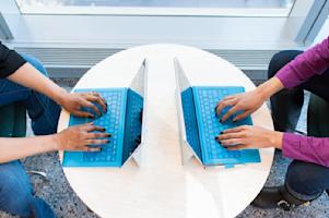 Two coworkers typing on their laptops on a shared table.