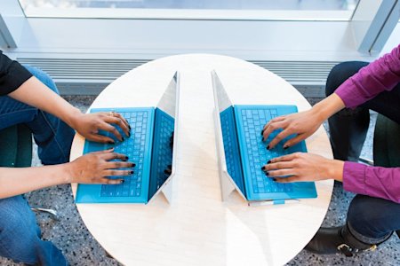 Two coworkers typing on their laptops on a shared table.