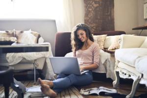 A woman with a laptop and sitting on the floor in a living room working remotely.