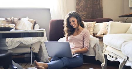 A woman with a laptop and sitting on the floor in a living room working remotely.