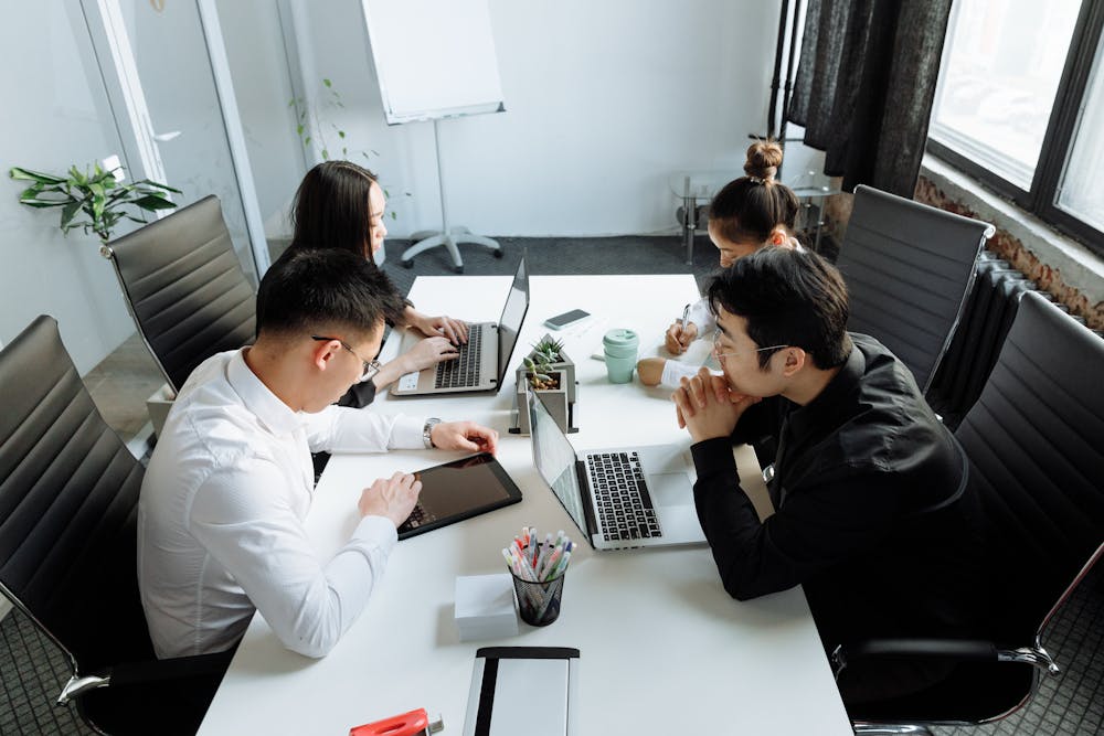 Coworkers using their computers and devices at a conference table.