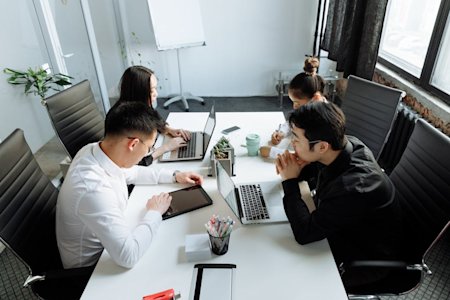 Coworkers using their computers and devices at a conference table.