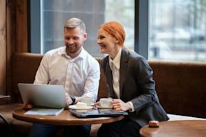 A man and woman working in a cafe looking at a laptop screen.