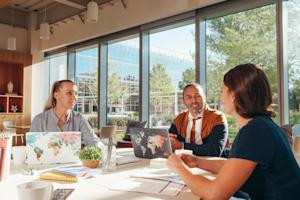 Co-workers sitting at a conference table in their office while working on their laptops.