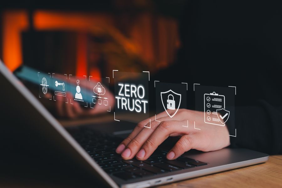A person types on a laptop keyboard with virtual cybersecurity icons and the words Zero Trust displayed above the keyboard, representing digital security concepts.