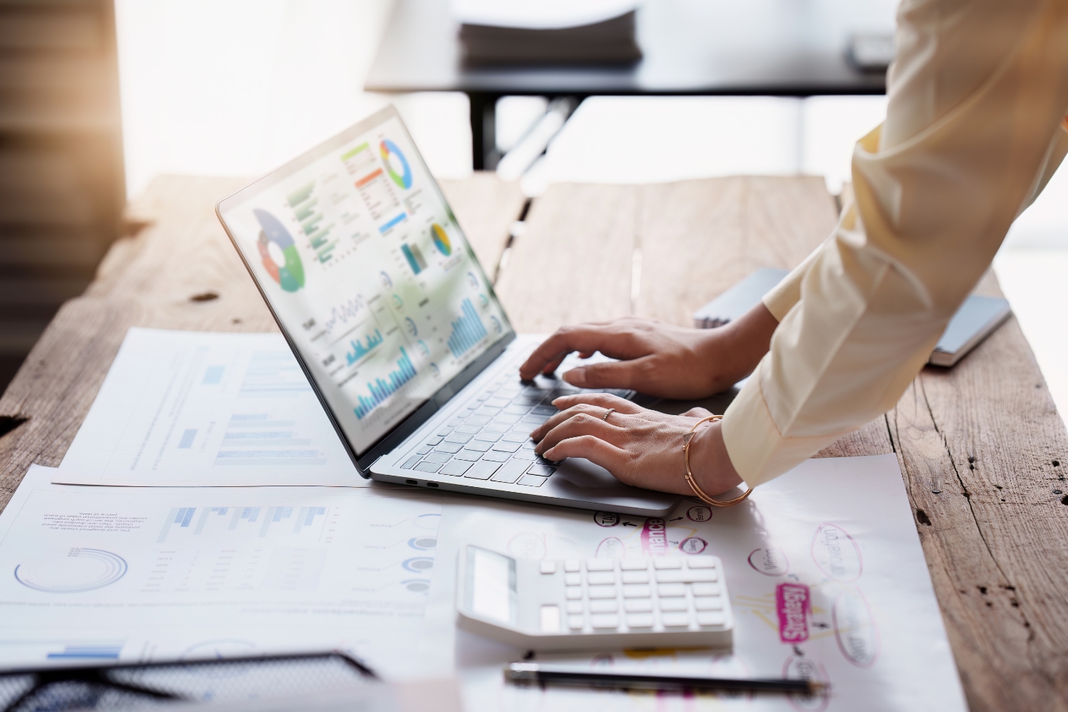 Person using a laptop with workflow management charts on a desk.