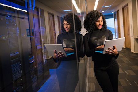 A woman standing in a server room working on her laptop.