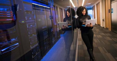 Woman standing in front of computer servers with her laptop in hand.