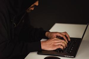 A person in a dark room typing on a laptop.