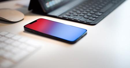 A phone on a desk next to a laptop and keyboard.