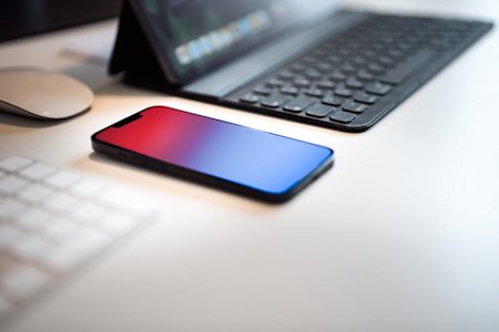 A phone on a desk next to a laptop and keyboard.