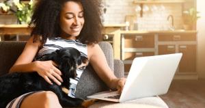 Woman sitting on a couch with her dog using a laptop