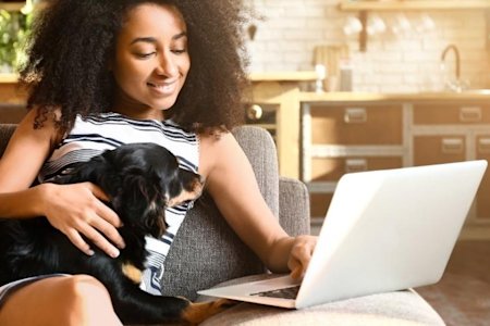 Woman sitting on a couch with her dog using a laptop