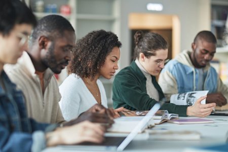 College students sitting at a table using laptops and books to study.