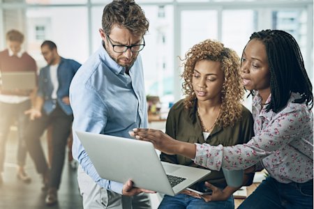 A group of professionals collaborating on a laptop, discussing IT incident response strategies in a modern office setting.