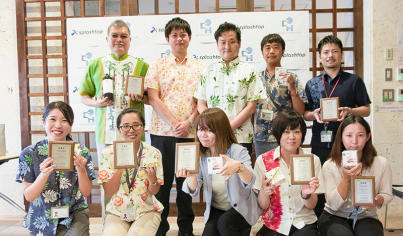 Splashtop team members smiling and holding awards, dressed in colorful attire with a Splashtop backdrop