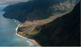 An uninhabited, deep green coast line meets a rich blue/green ocean.