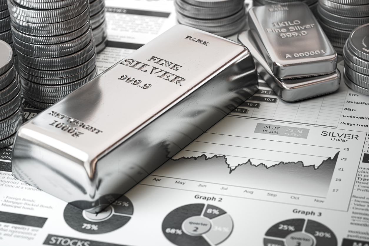 Silver ingots and coins lay atop a newspaper featuring a line chart 