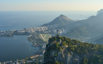 The iconic Rio de Janeiro statue, depicting a man in religious adornment with two arms outstretched horizontally, overlooks the city of Rio de Janeiro, Brazil