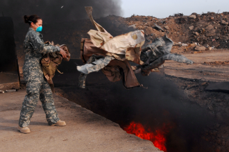 A US soldier tosses discarded US uniforms into an open burn pit at an unknown location in the middle east