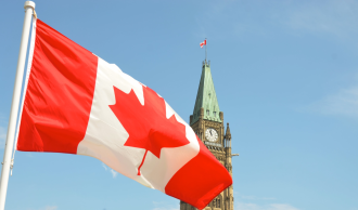 The Canadian flag flies in the foreground, in the background, a copper painted clocktower stands tall in an unknown location