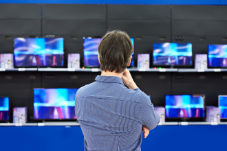 A man, back towards the viewer, appraises several different models of television inside a retailer 