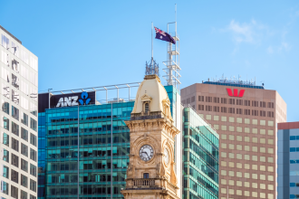 An aerial drone snapshot of an ANZ tower and a Westpac tower standing side by side with the Australian flag flying atop a clocktower in the foreground